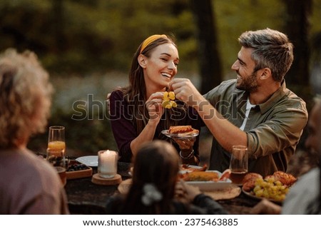 Beautiful happy couple enjoying their picnic with their family in the wood while eating grapes