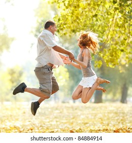 Beautiful happy couple jumping in the park and holding hands