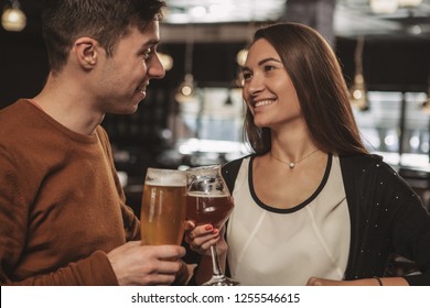 Beautiful happy couple looking at each other with love, celebrating their anniversary, having drinks at the restaurant together. Beautiful woman and her handsome boyfriend drinking craft beer - Powered by Shutterstock