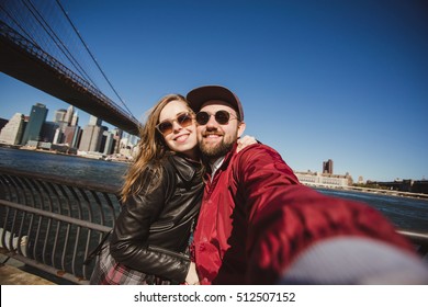 Beautiful happy couple taking selfie self-portrait on Brooklyn Bridge, New York. Hipster tourists having fun and photographing NY landmarks for travel blog. - Powered by Shutterstock