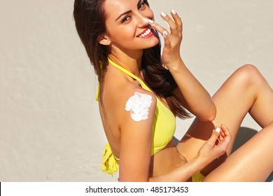 Beautiful happy cute woman applying suntan cream to her nose with beach  background