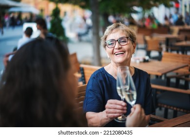 Beautiful happy elderly woman sitting with her friend in a street cafe clinking glasses - Powered by Shutterstock