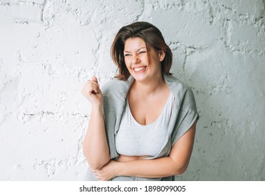 Beautiful Happy Emotional Brunette Young Woman Plus Size Body Positive In Comfortable Sport Wear Near The White Brick Wall