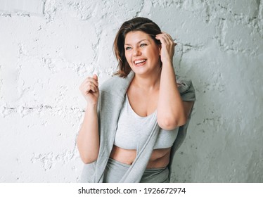 Beautiful Happy Emotional Brunette Young Woman Plus Size Body Positive In Comfortable Sport Wear Near The White Brick Wall