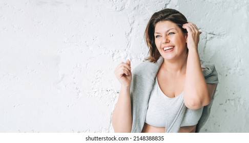 Beautiful happy emotional brunette young woman plus size body positive in comfortable sport wear near the white brick wall, banner - Powered by Shutterstock