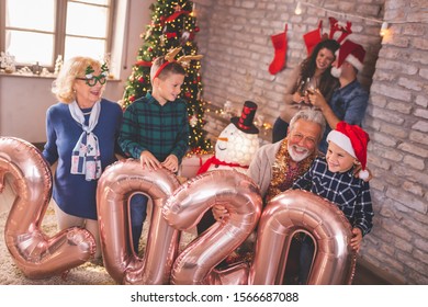 Beautiful Happy Family Celebrating Christmas At Home, Having Fun Holding Giant Balloons Shaped As Numbers 2020, Representing The Upcoming New Year