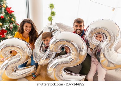 Beautiful Happy Family Celebrating Christmas At Home, Having Fun Holding Giant Balloons Shaped As Numbers 2022, Representing The Upcoming New Year