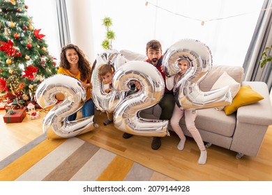 Beautiful Happy Family Celebrating Christmas At Home, Having Fun Holding Giant Balloons Shaped As Numbers 2022, Representing The Upcoming New Year