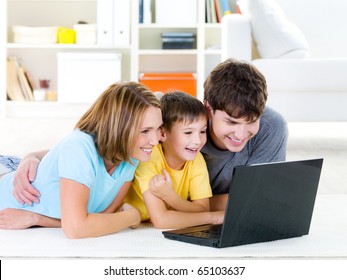 Beautiful Happy Family With Child Looking At Laptop With Cheerful Smile - Indoors