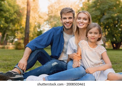 Beautiful happy family enjoying moment while sitting on blanket in park and looking at camera. Caucasian parents with small daughter relaxing in wood forest together