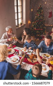 Beautiful Happy Family Gathered Around The Table, Having Christmas Dinner, Enjoying Their Time Together And The Winter Holiday Season