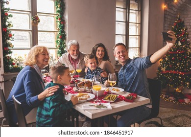 Beautiful happy family gathered around the table, having Christmas dinner, enjoying their time together and taking a selfie