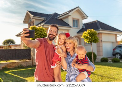 Schöne glückliche Familie, die Spaß dabei hat sich selbst mit Smartphone vor ihrem neuen Haus zu machen
