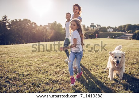 Beautiful happy family is having fun with golden retriever outdoors. Mother, father and daughter are running with dog labrador in park.
