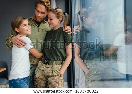 Beautiful happy family hugging and laughing while standing near window indoors