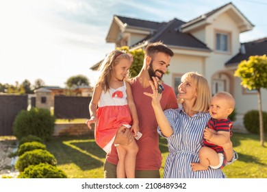 Beautiful happy family standing in front of their new house, parnets holding children and keys