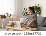 Beautiful happy female writer with laptop and books sitting on sofa at home