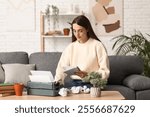 Beautiful happy female writer with typewriter, books and cup of tea writing in notebook on sofa at home