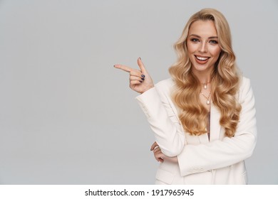 Beautiful happy girl in jacket smiling and pointing finger aside isolated over grey background