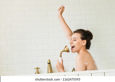beautiful happy girl singing and having fun in bathtub