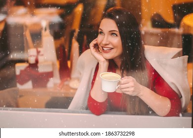 Beautiful Happy Girl In Stylish Coat Look In Window And Smile, Drink Morning Coffee In Restaurant. Cheerful Attractive Elegant Woman Enjoy Coffee In Cafe. Coffee Break, Winter Holidays Shopping