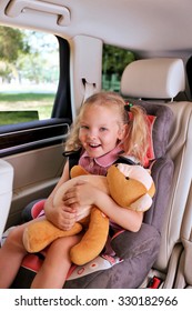 Schönes glückliches Mädchen mit Teddybär sitzend im Auto