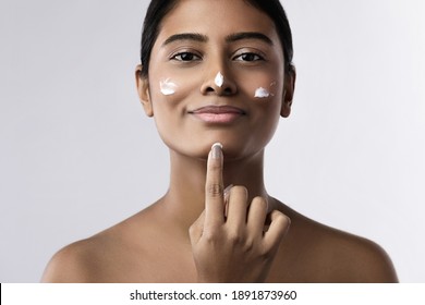 Beautiful and happy Indian woman applying moisturizing cream on her face