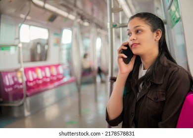 Beautiful happy Indian young woman talking on smart phone in the subway metro train.
