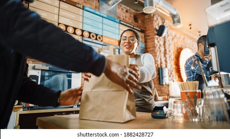 Beautiful Happy Latin Barista Serves Order to a Food Delivery Courier Picking Up Paper Bag with Pastries from a Cafe Restaurant. Delivery Guy Puts Food in His Hot Thermal Insulated Bag.