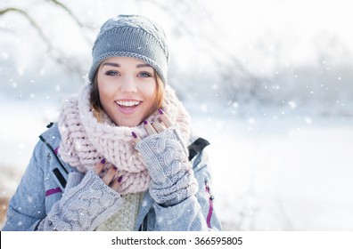 Beautiful  Happy Laughing Young Woman Wearing Winter Hat Gloves And Scarf Covered With Snow Flakes. Winter Forest Landscape Background