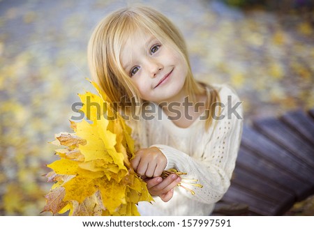 beautiful happy little girl has fun playing with fallen golden leaves in the autumn park