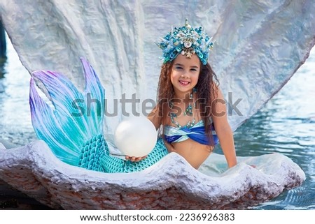 A beautiful happy little girl in a mermaid costume sits in a large sea shell