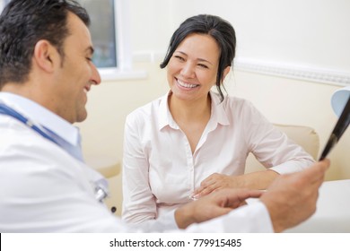 Beautiful Happy Mature Asian Woman Smiling Joyfully While Talking To Her Doctor During Medical Appointment At The Local Clinic. Therapist Examining MRI Or X-ray Scan While Talking To His Patient