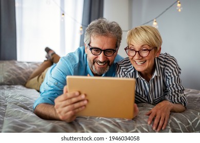 Beautiful Happy Mature Couple Is Using A Digital Tablet, Talking And Smiling At Home