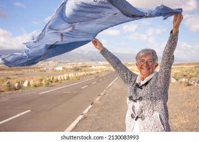 Beautiful Happy Mature Woman Outdoors In Countryside Looking At Camera Waving Scarf In The Wind. Smiling Caucasian Senior Woman With Short Hair Wearing Eyeglasses Enjoying Freedom