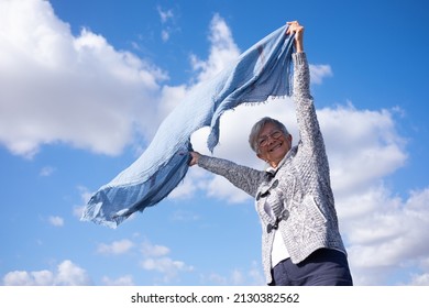 Beautiful Happy Mature Woman Outdoors Looking At Camera Waving Scarf In The Wind. Smiling Caucasian Senior Woman With Short Hair Wearing Eyeglasses Enjoying Freedom