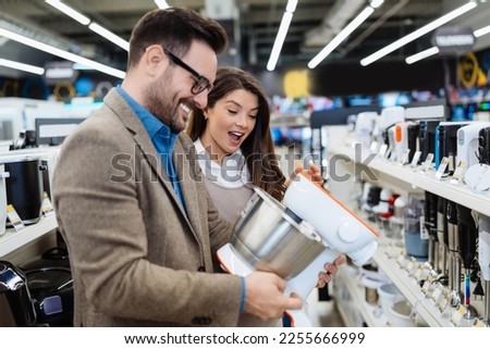 Beautiful and happy middle age couple buying consumer tech products in modern home tech store. They are choosing small kitchen appliances. People and consumerism concept.