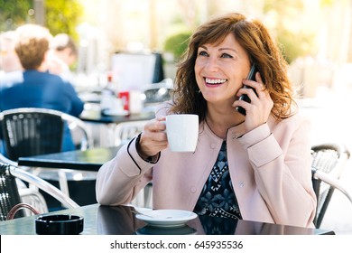 Beautiful And Happy Middle Aged Woman Having Coffee While Talking On Mobile Phone