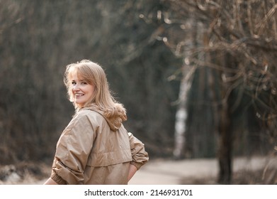 A beautiful happy middle-aged blonde woman in a beige jacket walks through a sunny spring or winter park. The woman looks around and laughs. Happiness and mental health.