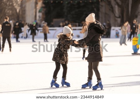 beautiful happy mother and daughter smiling at camera while standing together on skating rink.