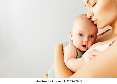 Beautiful Happy Mother Holds Her Baby On A Plain Light Background.