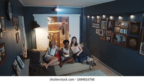 Beautiful Happy Multiethnic Women Friends Laugh Watching Comedy TV Show At Home On Big Screen With Projector Slow Motion