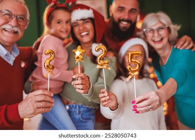 Beautiful happy multi-generation family celebrating New Year at home, having fun holding little balloons shaped as numbers 2025 - Powered by Shutterstock