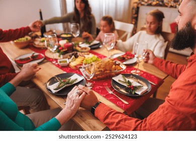 Beautiful happy multi-generation family gathered around the table, holding hands with eyes closed, praying before having Christmas dinner all together at home - Powered by Shutterstock