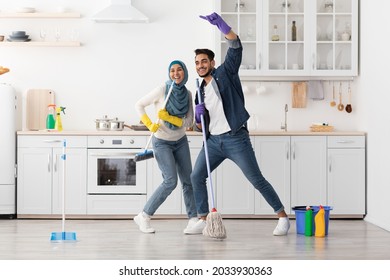 Beautiful Happy Muslim Young Couple Cleaning Floor And Having Fun In Kitchen Together, Full Length Photo, Copy Space. Funny Lady In Hijab And Her Singing Boyfriend House-keeping Their New House