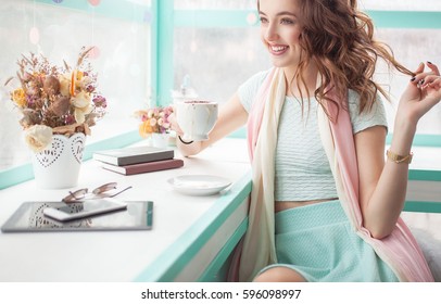 Beautiful Happy Pretty Young Woman Sitting In A Cafe With Tablet And Mobile Phone. Spring Trendy Pink And Blue Colors. Flowers And Books On The Table.