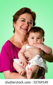 Beautiful Happy Senior Caucasian Hispanic Latina Grandmother Holding Cute Baby In Arms, On A Green Background.