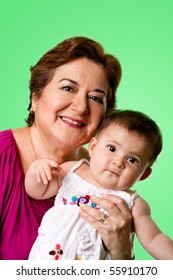 Beautiful Happy Senior Caucasian Hispanic Latina Grandmother Holding Cute Baby In Arms, On A Green Background.