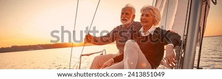 Beautiful and happy senior couple in love sitting on the side of sailboat or yacht deck floating in sea at sunset and enjoying amazing view, sailing together