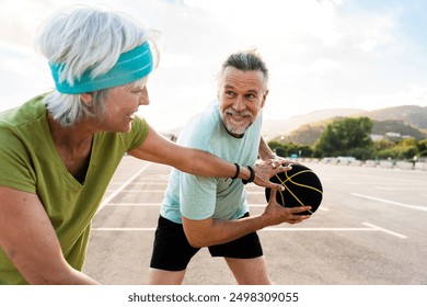 Beautiful happy senior couple playing basketball and having fun - Mature married couple in love bonding outdoors and doing sport together, concepts about elderly lifestyle, relationship and sports - Powered by Shutterstock